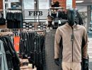 Arbeitskleidungsgeschäft mit schwarzen Kleiderständern und Schaufensterpuppe im Vordergrund