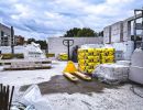 Baustelle mit Paletten voller Zementsäcke und Porenbetonblöcken, Hubwagen steht bereit unter Wolkenhimmel.