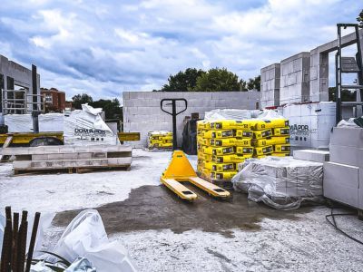 Baustelle mit Paletten voller Zementsäcke und Porenbetonblöcken, Hubwagen steht bereit unter Wolkenhimmel. Baustelle mit Paletten voller Zementsäcke und Porenbetonblöcken, Hubwagen steht bereit unter Wolkenhimmel.