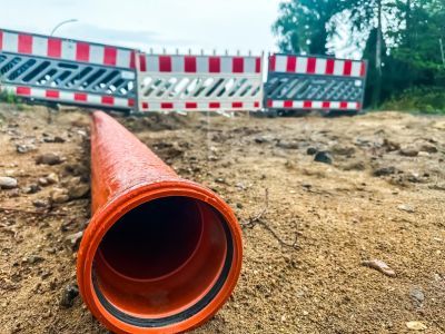Orange Rohrleitung liegt auf sandigem Boden vor Baustellenabsperrung mit rot-weißen Barrieren. Orange Rohrleitung liegt auf sandigem Boden vor Baustellenabsperrung mit rot-weißen Barrieren.