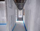Langer Rohbauflur mit unverputzten Wänden und freiliegenden Kabeln an der Decke, zeigt Innenausbauphase.