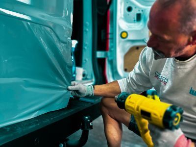 Folie wird mit Heißluft auf Fahrzeug geklebt – zeigt Fahrzeugveredelung durch moderne Werbetechnik Folie wird mit Heißluft auf Fahrzeug geklebt – zeigt Fahrzeugveredelung durch moderne Werbetechnik