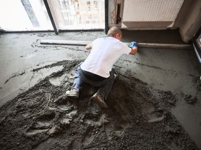 Person glättet frischen Betonboden mit langer Latte, ebene Fläche entsteht durch präzises Ausrichten im Innenraum