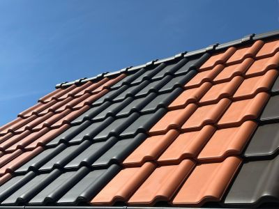 Dach mit Ziegeln in Rot, Grau und Braun unter blauem Himmel zeigt Vielfalt an Materialien für Dachdeckung