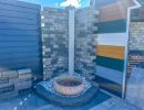 Steinbrunnen mit Wasserbecken vor gemusterter Mauer im Freien, dekoratives Element für Gartenbau sichtbar