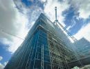 Hohes Gebäude eingerüstet, Kräne arbeiten daran, zeigt Fortschritt im Hochbau unter blauem Himmel mit Wolken