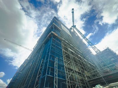 Hohes Gebäude eingerüstet, Kräne arbeiten daran, zeigt Fortschritt im Hochbau unter blauem Himmel mit Wolken