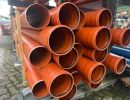 Gestapelte orange Kunststoffrohre lagern draußen, zeigen Materialien für unterirdische Infrastrukturprojekte