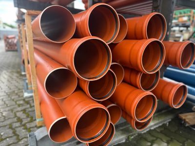 Gestapelte orange Kunststoffrohre lagern draußen, zeigen Materialien für unterirdische Infrastrukturprojekte