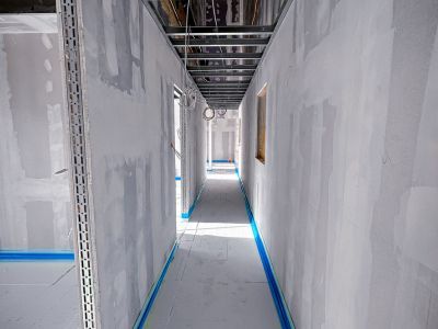 Rohbauflur mit unverputzten Wänden und Kabeln an Decke, zeigt Innenausbauphase mit sichtbarer Technikstruktur