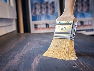 Pinsel  liegt auf dunklem Holz, zeigt Anwendung von Farben oder Lasuren im Innenbereich